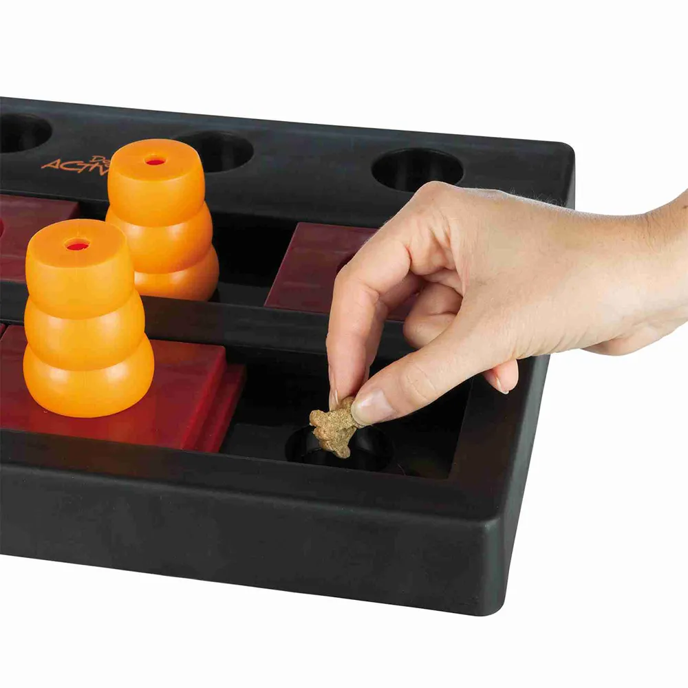 Detalle del juego Dog Activity Chess Nivel 3 con una mano colocando un snack en el compartimento, preparación del juego de inteligencia para perros.
